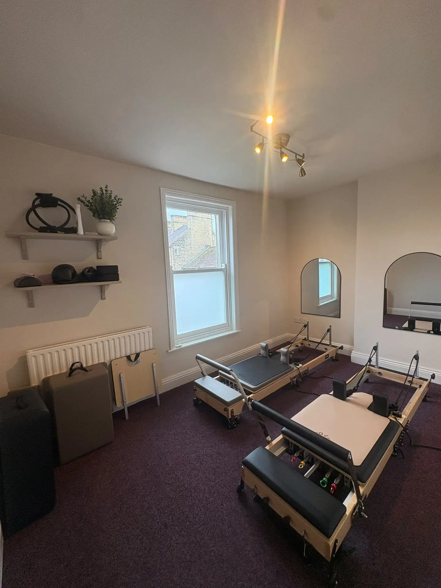 Reformer Pilates studio with two Reformer machines, arched mirrors and shelves of small equipment