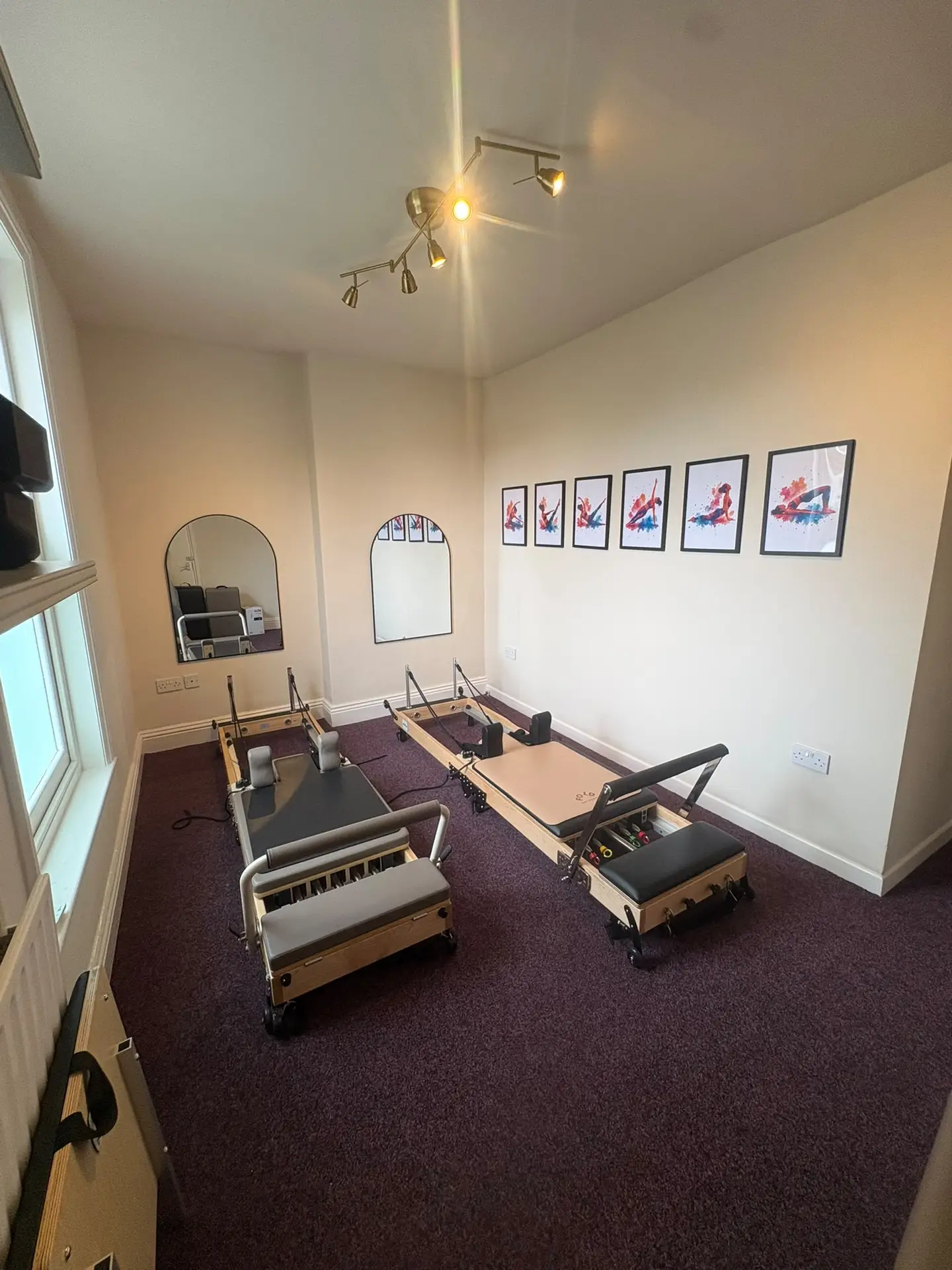 Two Reformer Pilates machines in a bright studio with arched mirrors and framed Pilates prints